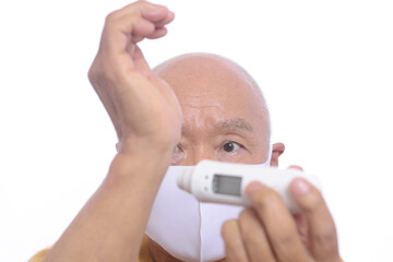 マスクをしている日本人シニア男性が検温をしている