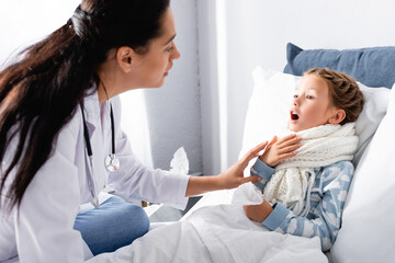 pediatrician examining sore throat of diseased girl lying in bed