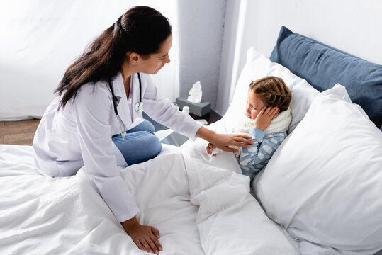 Doctor Touching Child Suffering From Pain In Ear While Lying In Bed