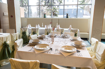 Indoor restaurant wedding tables beautiful decorated with candles , plates and cutlery prepared for the arriving guests