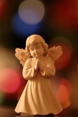 Statuetta natalizia di legno di un angelo che prega con sfondo bokeh di albero di Natale