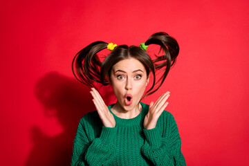 Photo of funny surprised young woman dressed green knitted sweater rising fists arms big eyes isolated red color background