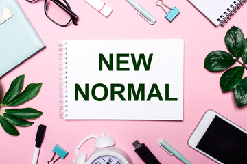 Fototapeta na wymiar NEW NORMAL is written in a white notebook on a pink background surrounded by business accessories and green leaves.
