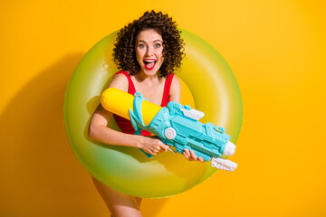 Photo of pretty good mood curly lady travel have best trip entertainment pool party hold bouy water gun wear trendy outfit isolated yellow color background