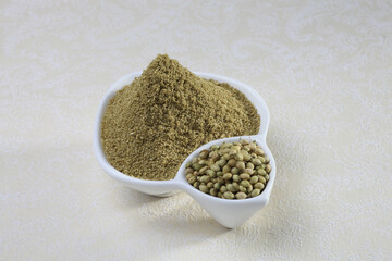 Coriander seeds and powder in a white ceramic bowl