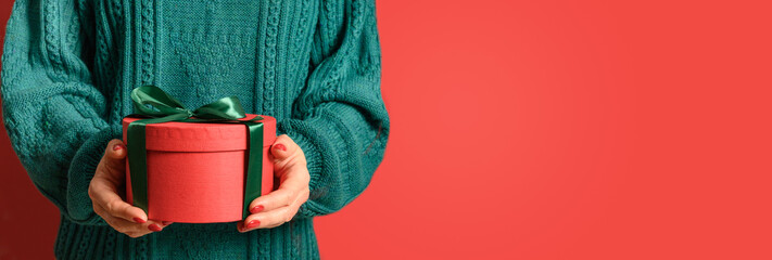 Christmas red gift in woman hands in cozy green sweater. Xmas festive banner with copy space.