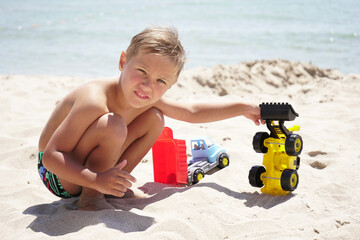 Happy baby playing with cars on the beach, on the horizon azure sea and blue sky.