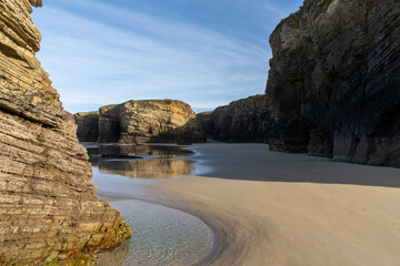 Fototapeta na wymiar sandy beach with tidal pools and jagged broken cliffs behind in warm evening light