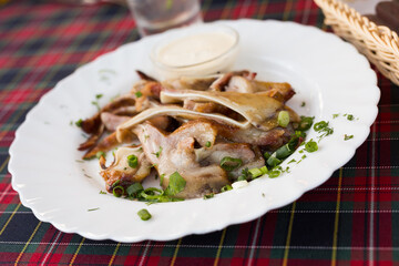 delicious smoked pork ears served with sour cream and herbs on a white plate in a restaurant