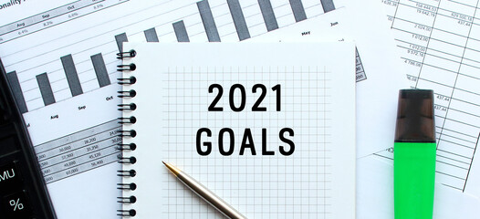 Text 2021 GOALS on the page of a notepad lying on financial charts on the office desk.
