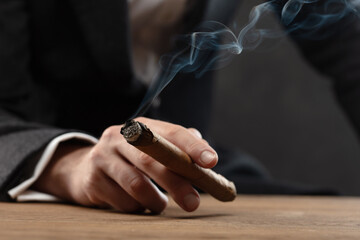Close-up of man's hand resting on table  holding a lit cigar