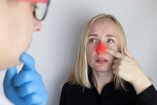 A young woman touches her nose, which is very painful. Medical care concept for difficulty breathing, clogged nasal passages and flu, colds or coronavirus. On examination by a doctor.