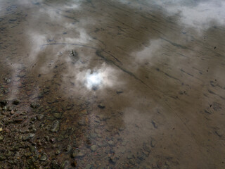 Detail from the Sava river, river bank and bed and reflection of clouds and sun in the water.