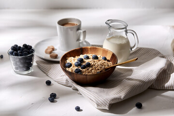 food, eating and breakfast concept - oatmeal in wooden bowl with blueberries, milk in glass jug and cup of coffee with brown sugar on kitchen towel