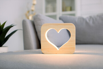 Close up of wooden night lamp with heart picture, on gray sofa, at stylish light home living room...