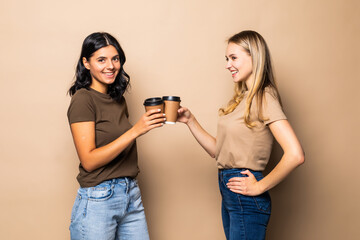 Young two women drinking take away coffee on beige background
