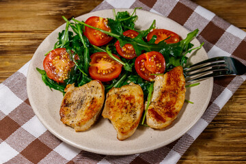 Fried chicken breast with salad of fresh arugula and cherry tomatoes on wooden table