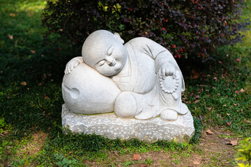 A small statue of a little monk sleeping at a garden in historic Buddhist Jinshan Temple, Zhenjiang, Jiangsu, China.