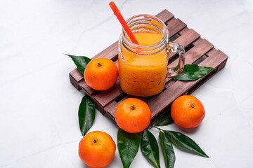 Closeup of fresh mandarin juice in a glass jar with a plastic reusable straw on a wooden tray
