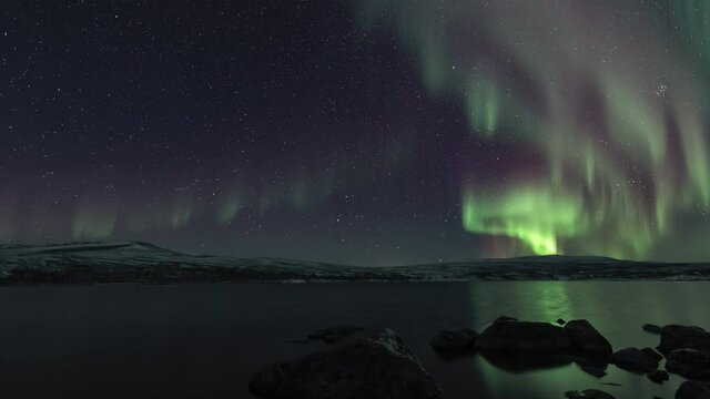 Auroras above a lake in Lapland, rocks on the foreground, tilt up
