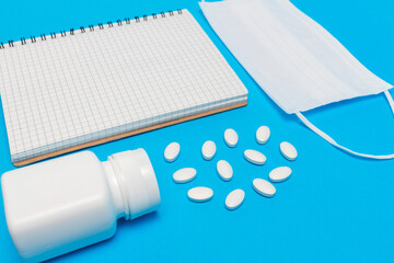 White medical mask, bottle with pills and notepad on blue background. Concepts of protection, prevention and treatment coronavirus, covid 19, flu
