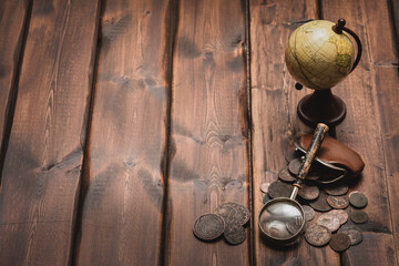 Obraz na płótnie Canvas Old ancient coins and magnifying glass on the brown wooden table background