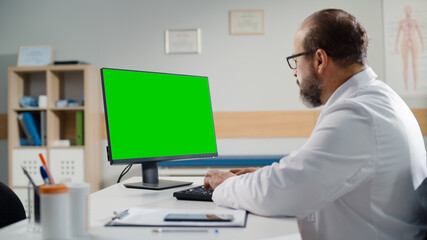 Latin Doctor's Office: Experienced Physician Sitting at His Desk Working on Green Chroma Key Screen...