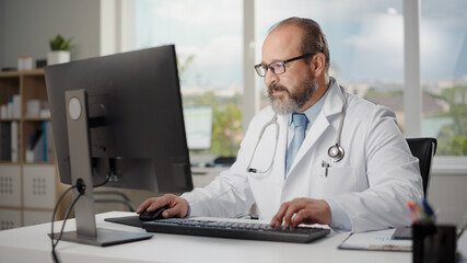 Hispanic Doctor's Office: Experienced Physician Sitting at His Desk Working on Personal Computer....