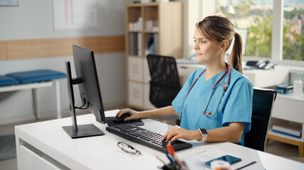 Hispanic Doctor's Office: Experienced Head Nurse Sitting at Her Desk Working on Personal Computer. Medical Health Care Specialist Filling Prescription Forms, Checking Analysis Test Results. High Angle