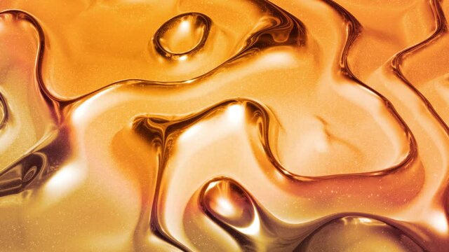 Looped abstract background with wavy sparkling golden liquid pattern on shiny glossy surface. Viscous yellow fluid like surface of gold foil or brilliant glass. Beautiful creative festive backdrop.