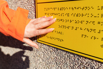 A woman's hand reads a yellow Braille sign. Close up. Concept of the day of the blind and disability
