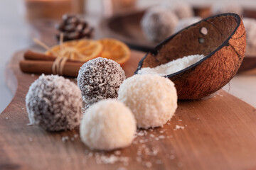 Homemade brownies and white chocolate with coconut flour and cookies on wooden desk with pine cone, orange and cinnamon sticks decoration, burning candles. White wooden table. Soft focus background