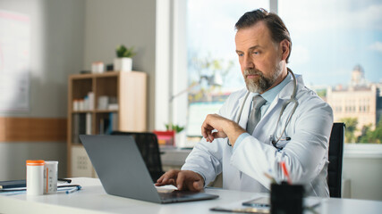 Obraz premium In a Doctor's Consultation Office: Experienced Physician Working on a Laptop, Thinking Over Diagnosis, Prescribing Medicine, Analysing Tests Results. Health Care Specialist Planning Treatment