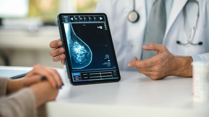 In a Doctor's Consultation Room: Friendly Professional Doctor Uses Digital Tablet Computer to Show Breast Scan to a Female Patient and Explains Importance of Breast Cancer Prevention. Focus on Tablet