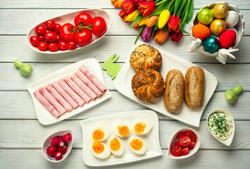 
Fresh crusty loaves of bread and bun with ham, eggs, tomatoes, radish and mug of tea on white...