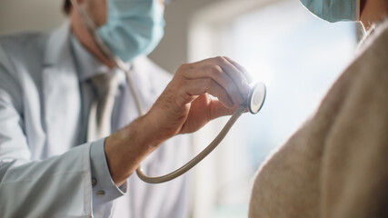 Doctor's Consultation Office: Physician Uses Stethoscope to Listen to Heartbeat and Lungs of the Female Patient. Medical Health Care. Both Wearing Face Masks. Close-up Shot with Focus on Stethoscope.