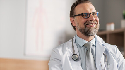 Doctor Consultation Office: Experienced Physician Wearing Glasses Sitting at His Desk and Smiling Charmingly. Health Care Specialist Talking about Health and Checking Test Results.