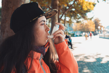 Chronic disease. Portrait of a teenage girl using an inhaler on the street, having an asthma attack. Side view. Outdoor - obrazy, fototapety, plakaty