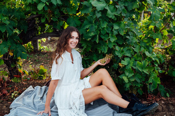 beautiful woman in white dress drinks from a glass of wine at a picnic in the vineyard