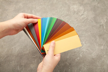 Female hand holding color trend palette on grey concrete background. Flat lay, top view.