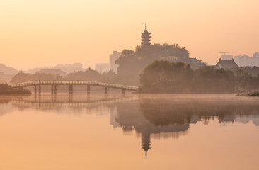 Sunrise view of symbolic Cishou Pagoda, Jinshan Temple, bridge amid fog with beautiful reflection on Jinshan Lake in Zhenjiang, Jiangsu, China. Tourist attraction.