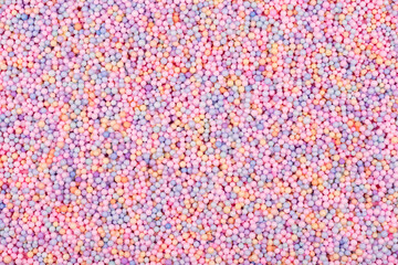 Pastel color balls texture. Styrofoam or Polystyrene foam background. Mix of colorful sugar balls, used to decorate baking and sweets. Rainbow colored sugar chips or dragee spins, confectionery