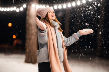 Beautiful young woman Playing with snow evening in the winter park. Happy  woman having fun on winter holidays. Christmas, New year. Winter lifestyle.