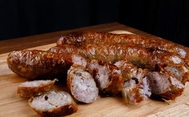 Homemade fried sausages and pieces of sausage on a wooden cutting board.