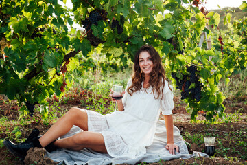 beautiful woman in white dress drinks from a glass of wine at a picnic in the vineyard