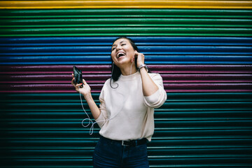 Excited Asian user with cellular device in hand grinning at publicity area satisfied with free time...