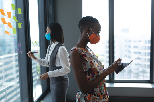 African american woman wearing face mask using digital tablet at modern office