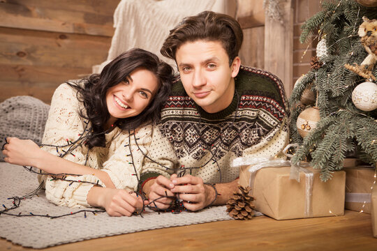 Beautiful brunette caucasian romantic loving couple in cozy warm sweaters in the cabin on a christmas new year eve, smiling, kissing, having fun with each other. Dim dark night light, toned image