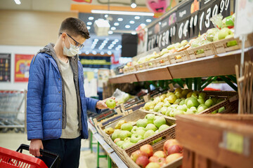 Teenager wearing protective mask picks fruits at grocery store