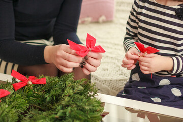 Daughter and mother make a Christmas wreath. Little girl helps to make a wreath. New Year's...